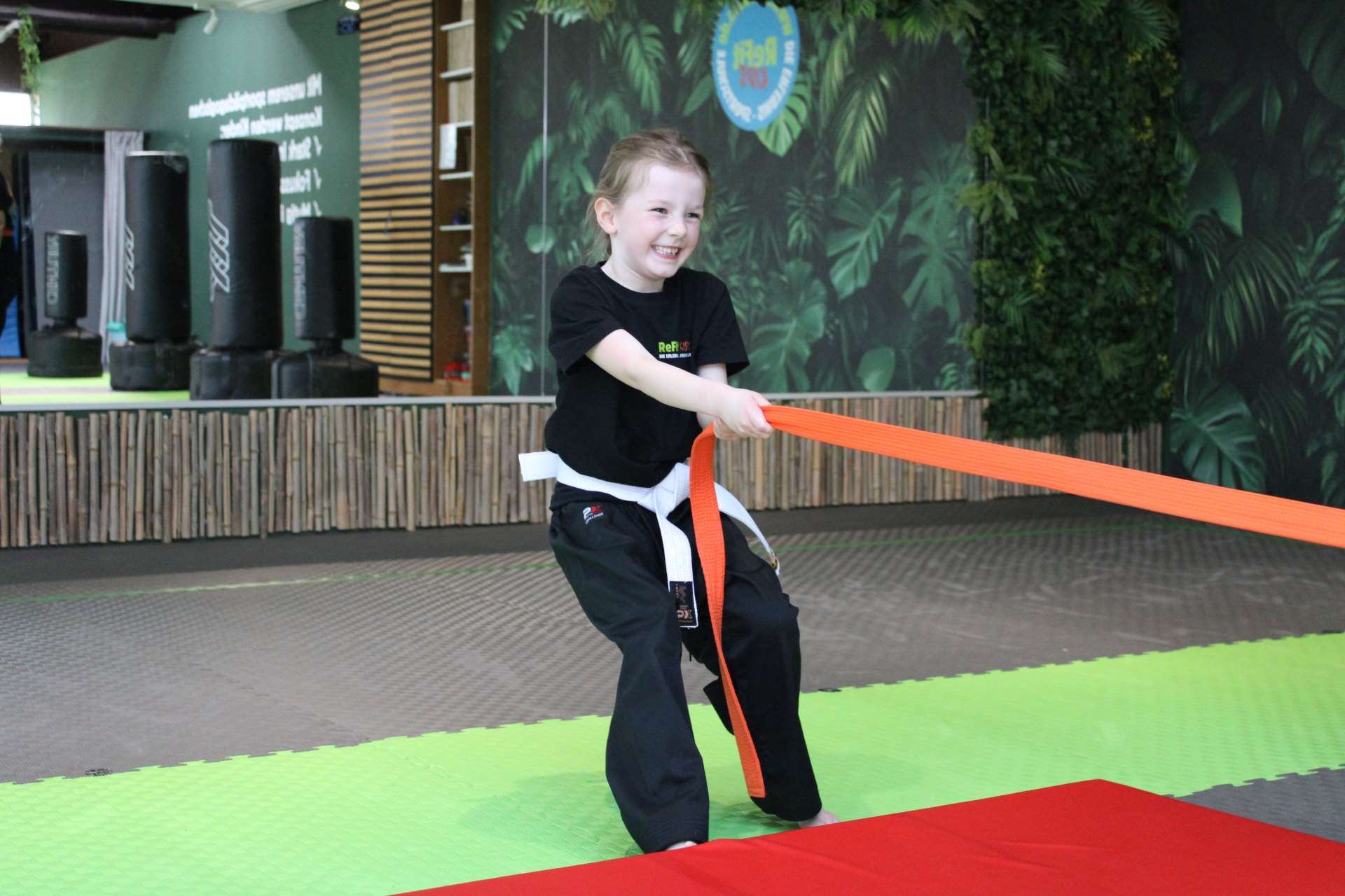 Lachendes Kind zieht am Widerstandsband im ReFit Kids Unterricht