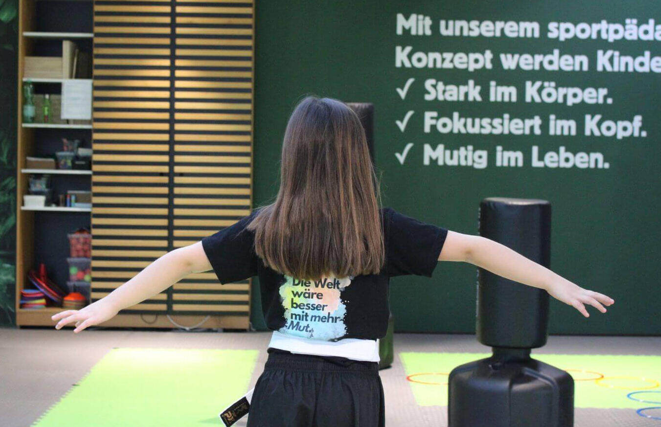 Kind steht mit ausgebreiteten Armen in der ReFit Kids Halle — Stark im Körper, Fokussiert im Kopf, Mutig im Leben