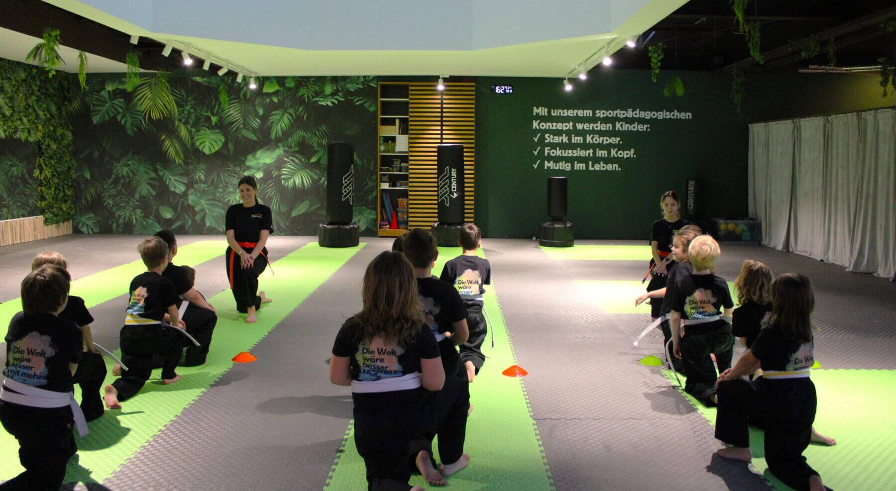 Gruppentraining — Kinder knien im Kreis mit zwei Coaches in der ReFit Kids Halle